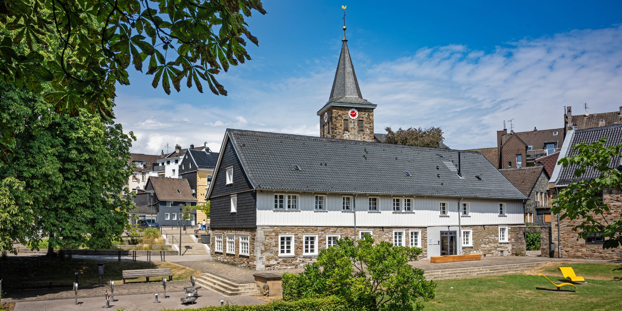 Historisches Gebäude mit Kirchturm im Hintergrund und grüner Wiese.