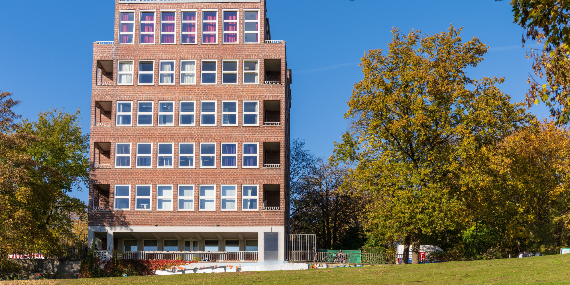 Buntes Schulgebäude mit Fensterfront und Bänken davor, Rasenfläche im Vordergrund 